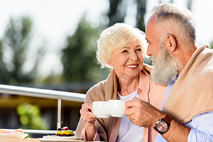 Elderly couple sitting outside smiling and drinking a cup of coffee