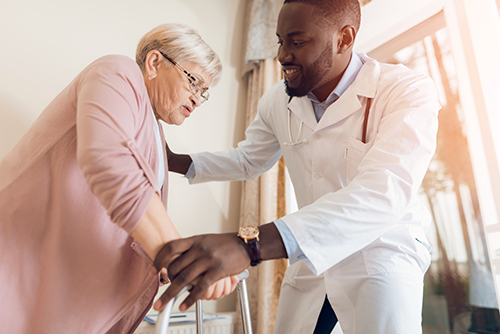 Male doctor assisting elderly woman with walker