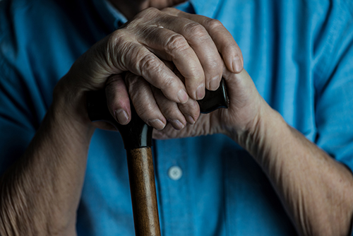 Close up of elderly person's hands resting on top of a walking cane